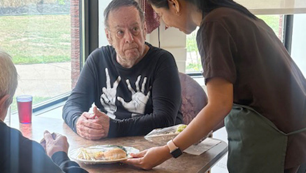 photo: woman serving lunch to two elderly men